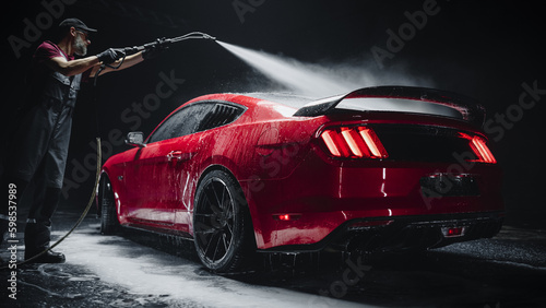 Car Wash Expert Using Water Pressure Washer to Clean a Red Modern Sportscar. Adult Man Washing Away Dirt  Preparing an American Muscle Car for Detailing. Creative Cinematic Footage with Luxury Vehicle