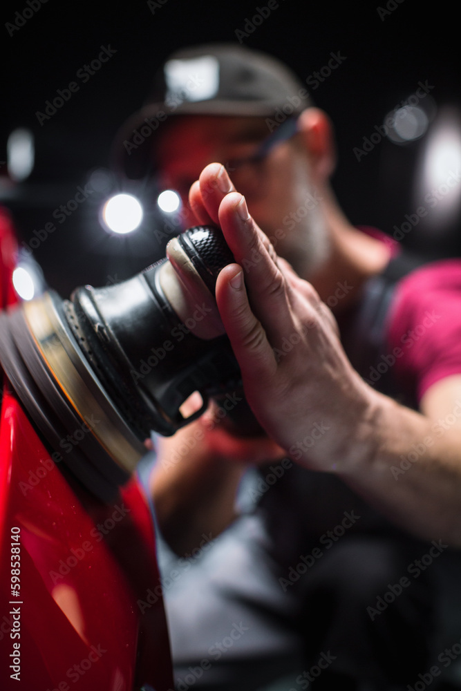 Naklejka premium Portrait of an Adult Man Working in a Detailing Studio, Prepping a Factory Fresh American Sportscar for Car Care Treatment. Technician Polishing the Fender with a Polishing Machine