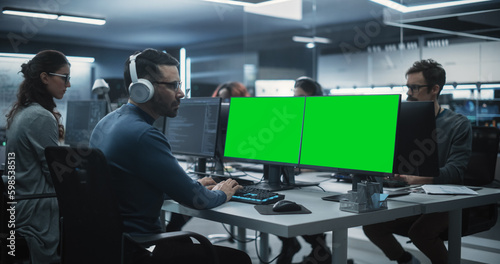 Group of Diverse Multicultural Men and Women Working on Desktop Computers in a Research Center. Young Software Developer Working on a Computer with Two Green Screen Mock Up Displays