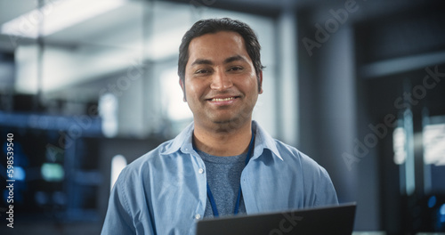 Handsome Smiling IT Specialist Using Laptop Computer in Data Center, Looking at Camera. Successful South Asian Businessman and e-Business Entrepreneur in Software Development Agency © Gorodenkoff
