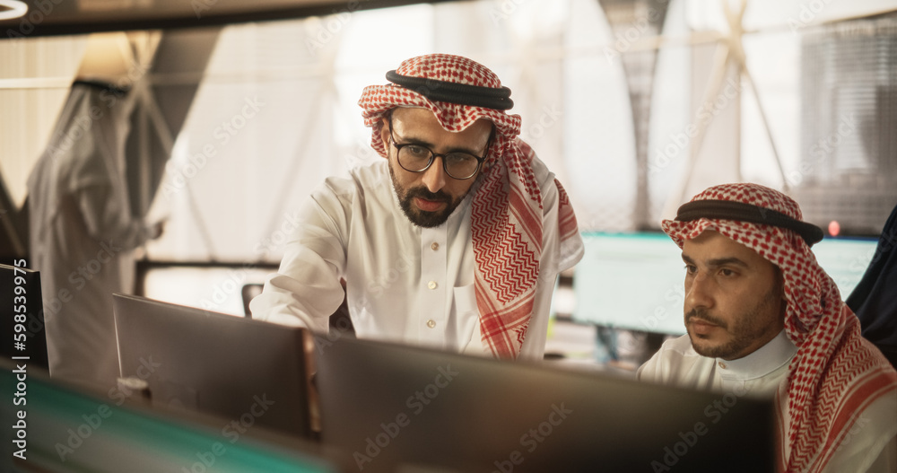 Arab Graphic Designer Working on Computer, Discussing Project with Team Leader. Middle Eastern Colleagues Working in Modern Office, Wearing Traditional White Thobes and Kaffiyeh