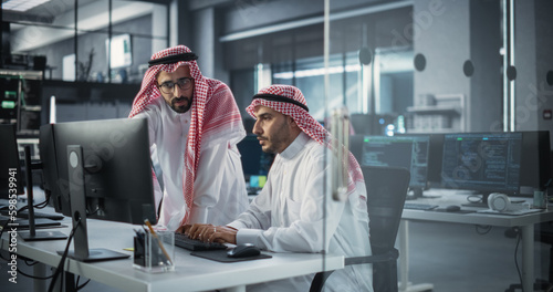 Bild auf Leinwand Two Young Saudi Software Engineers Use Desktop Computer to Discuss a Technological Project in a Modern Industrial Office