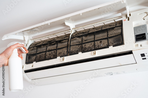 Картината върху платно A man's hand sprays a cleaning liquid on the moldy filters of an air conditioner