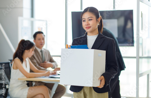 Asian professional successful new recruitment female employee businesswoman in formal business suit smiling standing moving in holding cardboard box containing paperwork document folder into office