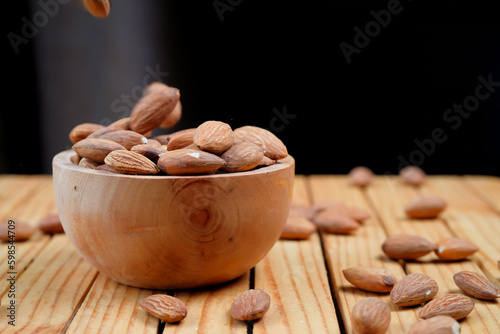 Peeled almonds in a wooden bowl and some scattered nuts on black background	
