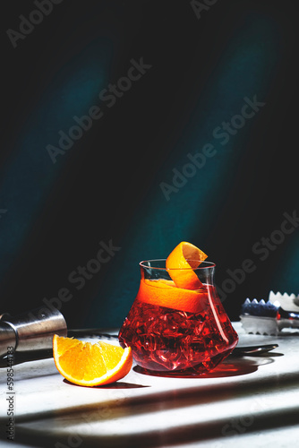 Boulevardier alcoholic cocktail drink with bourbon, vermouth, bitter, orange zest and ice. Dark green background, hard light, shadow pattern photo