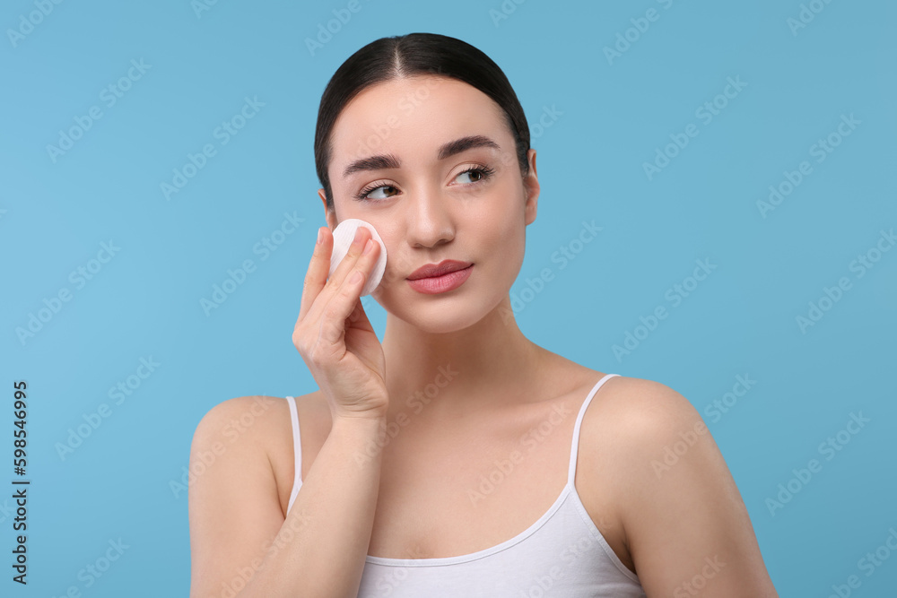 Beautiful woman removing makeup with cotton pad on light blue background Beautiful woman removing makeup with cotton pad on light blue background