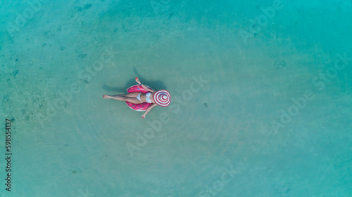 Aerial view with woman in bikini sunbathing as laying on swim ring  as blue sea water in background © SASITHORN