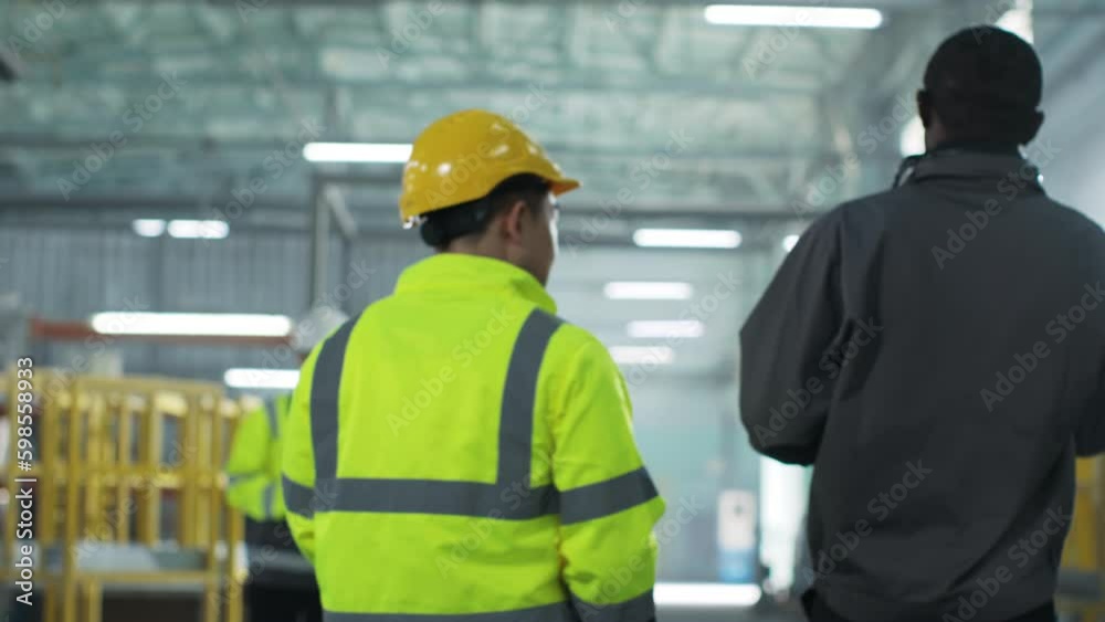 Two multicultural men walk from back at construction site. Smooth transition from employees to lead engineers discussing project. People in uniform at workplace. Ethnic diversity. Two multicultural men walk from back at construction site. Smooth transition from employees to lead engineers discussing project. People in uniform at workplace. Ethnic diversity.