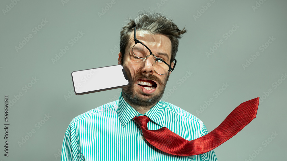 Expressive sad man, businessman in tie taking punch in face by flying smart phone. Concept of personal problems, financial loses, business fall - obrazy, fototapety, plakaty 