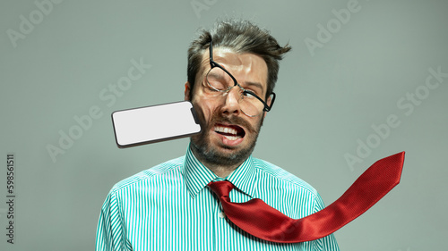 Fotografia Expressive sad man, businessman in tie taking punch in face by flying smart phone