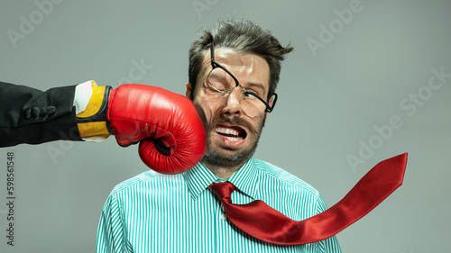 Mature man, businessman in red tie getting boxing punch in jaw from business competitors over grey background. Concept financial loses, business fall, deadlines, economic crisis