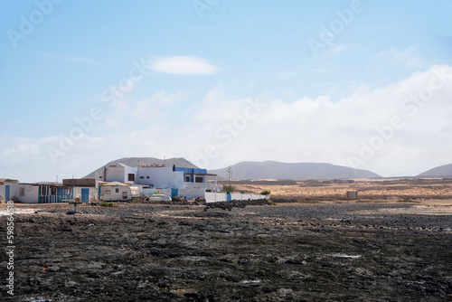View of Majanicho village in the touristic Fuerteventura, with small houses facing the sea at low tide and the sea rocks in sight during a clear day in the Canary Islands.