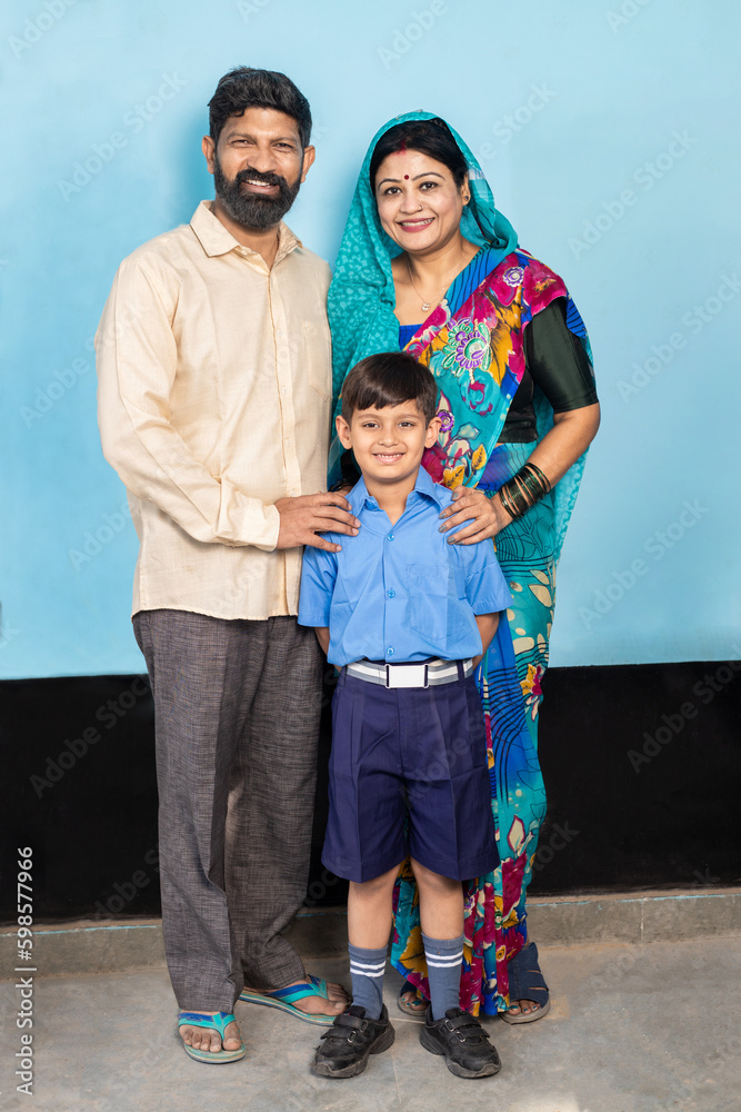 Fototapeta premium Young happy indian parents standing with little son wearing school uniform. Rural india, Education concept.