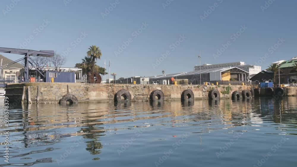 Cape Town harbour viewed from water, with people walking along stone wall jetty.