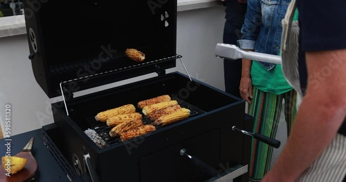 Multi generational people doing barbecue during weekend day at home's rooftop - Young man cooking corn cobs on the girll - Summer and food concept photo