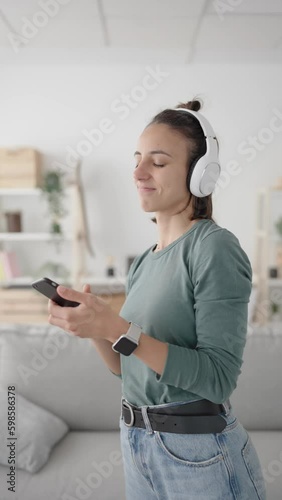 Young hispanic woman searching music on phone scrolling screen, and then dancing and listening music on headphones