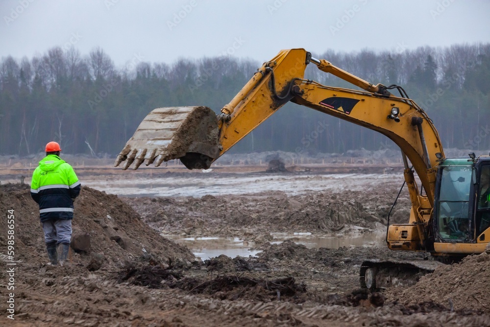 Ust-Luga, Leningrad oblast, Russia - November 16, 2021: Worker controls the excavator working. Flattening the landscape, groundworks