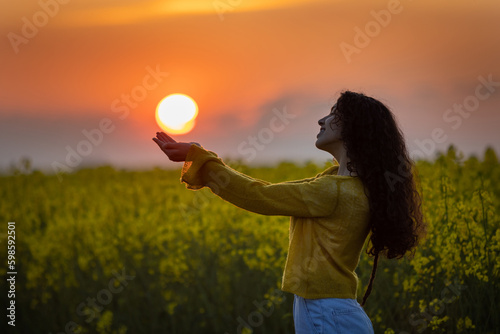 Girl holding sun in hands in rapeseed field photo