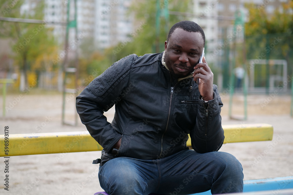 African american man sits at sport ground and speaks on smartphone African american man sits at sport ground and speaks on smartphone