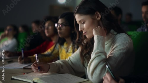 Talented Smart Female Student Studying in College with Diverse Multicultural Colleagues. She is Writing Down a Summary from the Lecture in Her Notebook