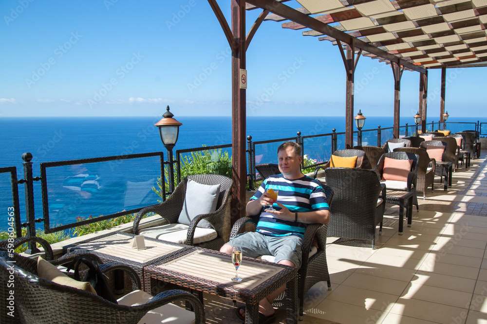 Rest of a man in summer clothes in an armchair hotel terrace overlooking the sea.