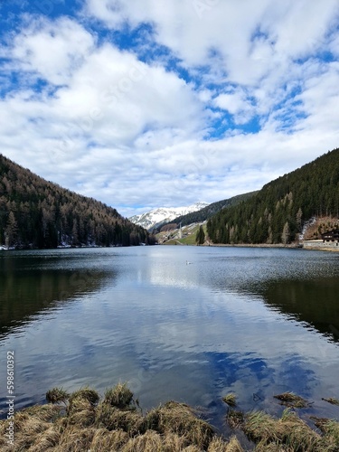 Fototapeta Naklejka Na Ścianę i Meble -  
Lago di Valdurna or Durnholzer see with swan swimming in the lake and reflection of snow capped mountain in the water, surrounded by lush green forest