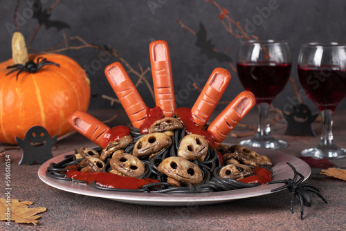 Themed food for Halloween - bloody hand from sausages with ketchup, mushrooms form of skulls and black spaghetti © Anzhela