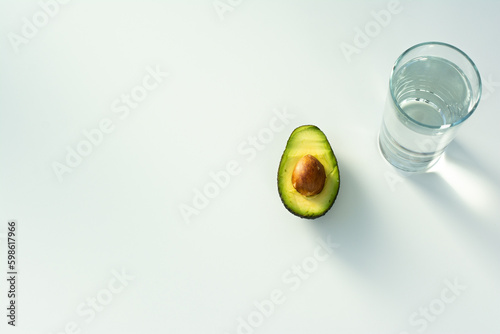 fresh ripe cut avocado halves and clean water in a glass on white table, healthy eating concept