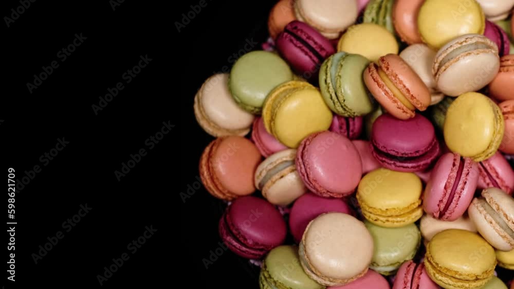 Top view of rotating fresh macaron cookies. Traditional french desserts from almond dough. Colourful sweet macaron cakes rotating against black background with copy space. French sweets concept.