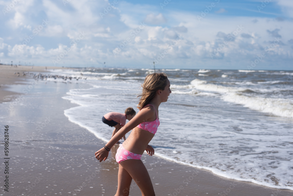 Naklejka premium A young boy and girl playing in the waves of the sea during a warm day during a summer vacation.