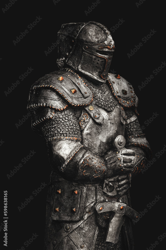 Statue of medieval knight in metal armor with a sword, isolated on dark black background Statue of medieval knight in metal armor with a sword, isolated on dark black background
