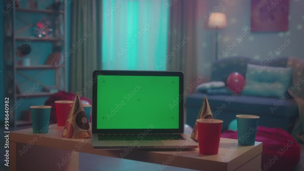 Laptop with green screen display in front of a room decorated for a house party. On a blurred background, lights flash and a disco ball sparkles. Advertising area, workspace mock up. Laptop with green screen display in front of a room decorated for a house party. On a blurred background, lights flash and a disco ball sparkles. Advertising area, workspace mock up.