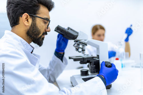 Male scientist working with microscope, doctor's team in laboratory doing research