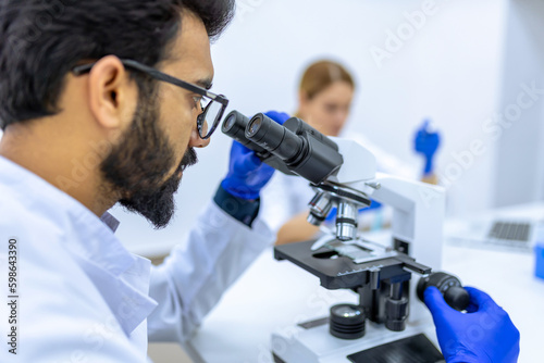 Male scientist working with microscope, doctor's team in laboratory doing research