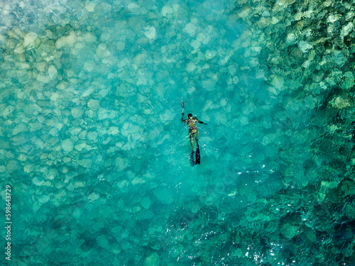 Aerial drone view of a person doing spearfishing on crystal blue water. Recreational fishing and summer activity. Summertime. 