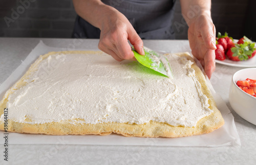 Woman spreads whipped cream on a sponge cake base for making a cake roll