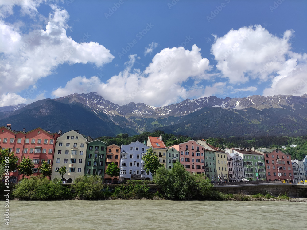 River view. A view on a river Inn, colorful houses and Tirol peaks. Innsbruck. Austrian Alps. Spring sunny day, blue sky and clouds. Remaining snow on the mountain.