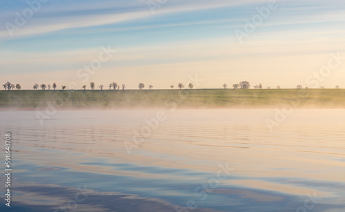 Fog on pond with tree on horizon under sunrise sky. Czech spring landscape