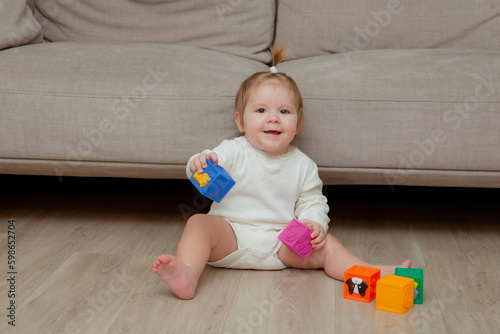 baby girl sitting at home on the floor playing cubes, child development © Olesya Pogosskaya