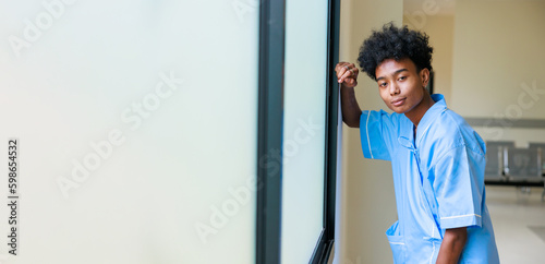 Unhappy lonely depressed and sad feeling. Black man patient standing by windows and look outside at medical center.