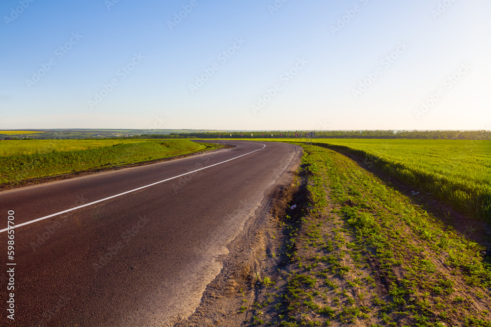 asphalt road turn among green rural fields