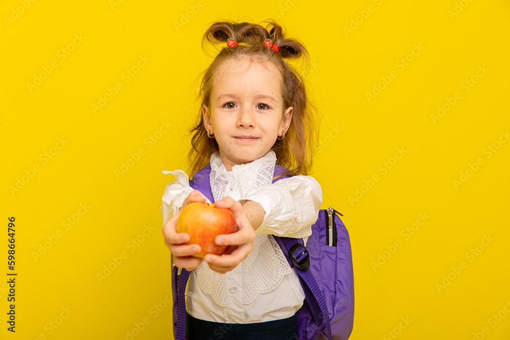 School Nutrition. Smiling Schoolgirl with school bag holding fresh apple and posing On Yellow Background. Studio Shot. School lunch concept