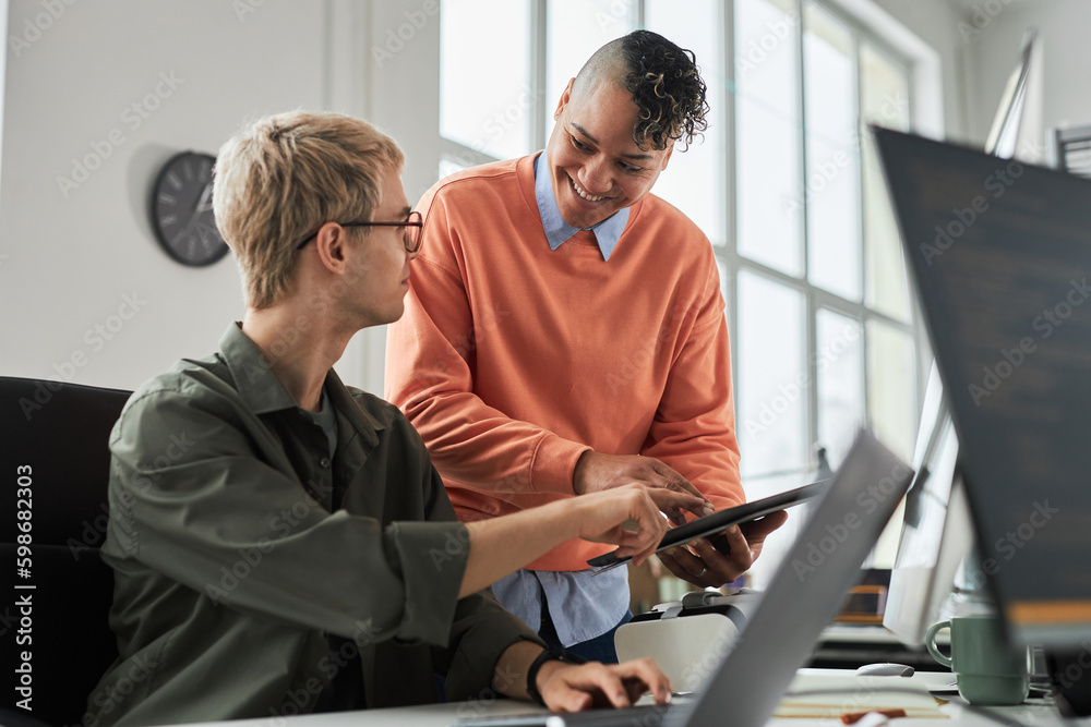 Smiling young colleague consulting with programmer about new software on digital tablet during their work in office Smiling young colleague consulting with programmer about new software on digital tablet during their work in office