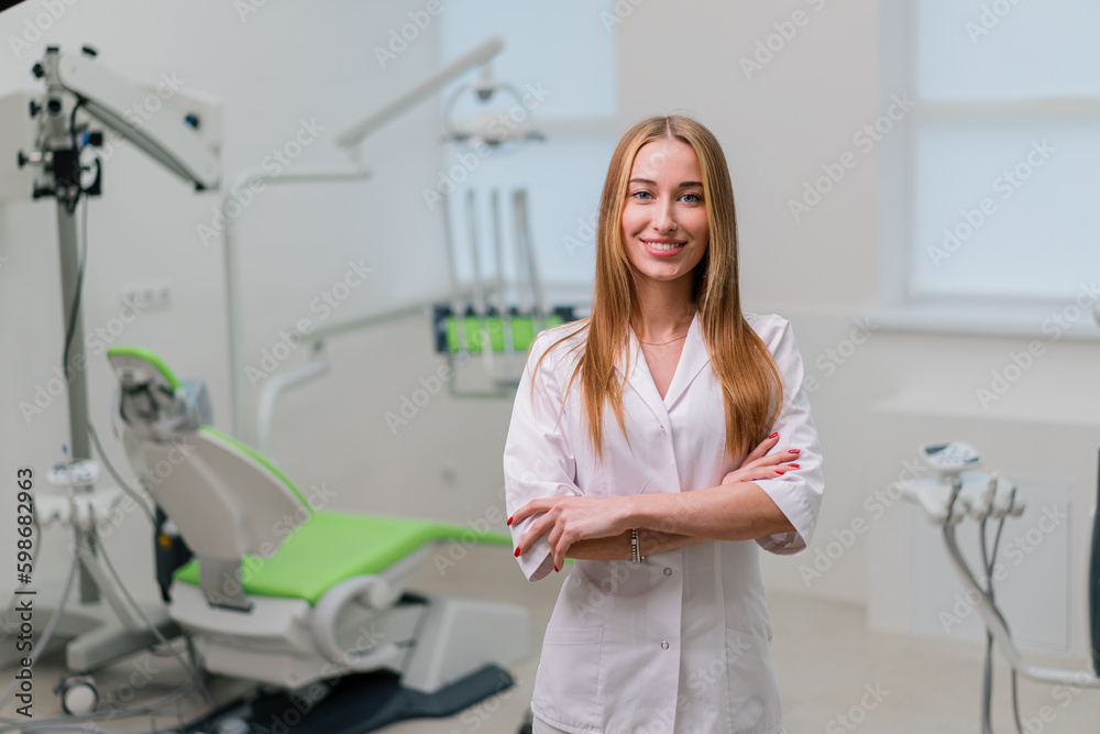 Obraz premium portrait of a beautiful young smiling doctor dentist standing in the dental office before the procedure