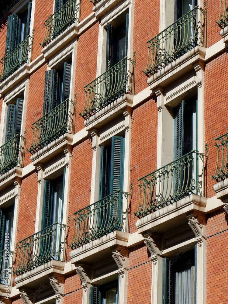 Vibrant facade of aged residential building made of red bricks with shuttered windows. Outside view, vertical photo