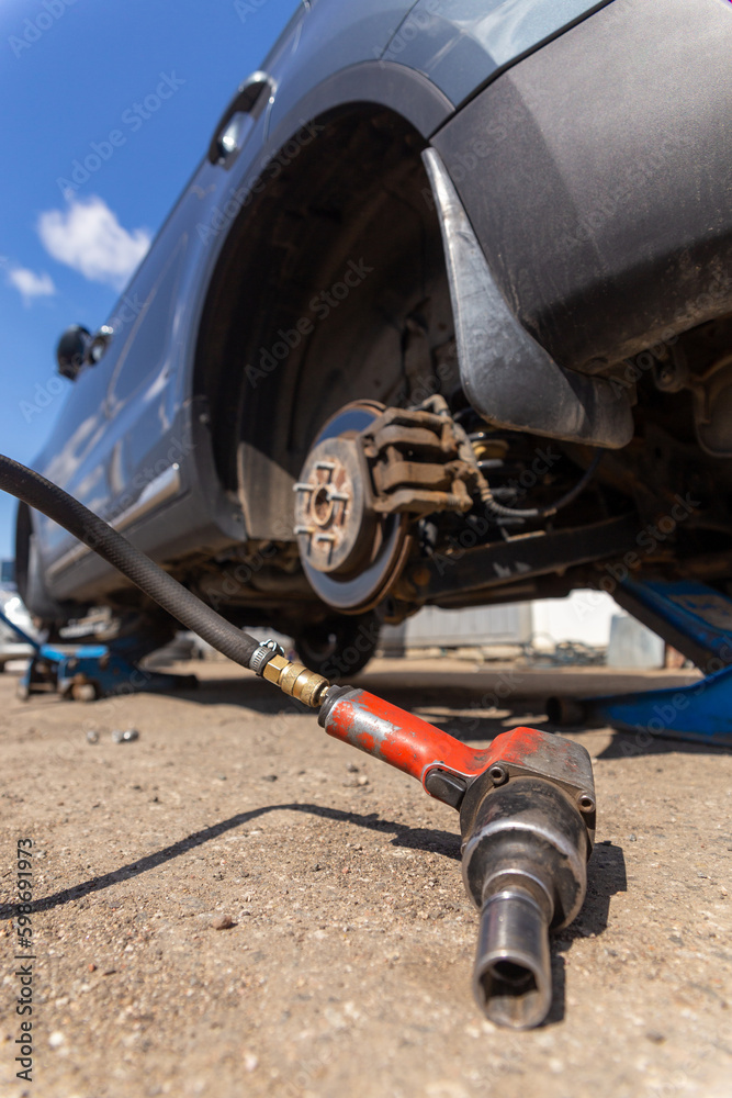 Pneumatic wrench tool on the asphalt and a car jack for lift up the body and changing the tire. Car without wheel Pneumatic wrench tool on the asphalt and a car jack for lift up the body and changing the tire. Car without wheel