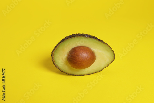 Half of a hass avocado with a stone on a yellow background