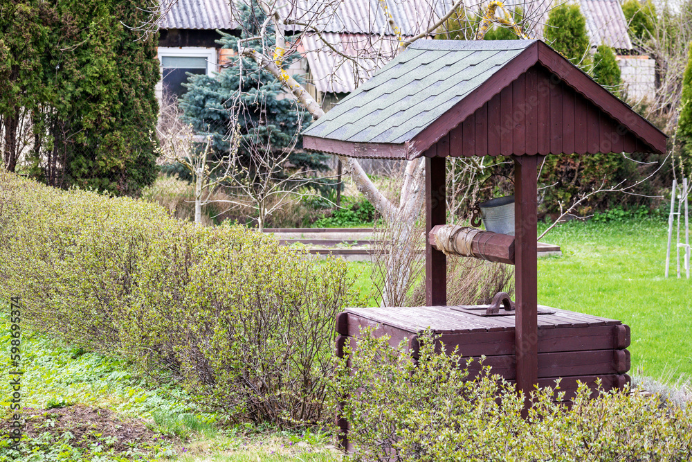 A wooden water well with a green roof sits in a garden. A wooden water well with a green roof sits in a garden.