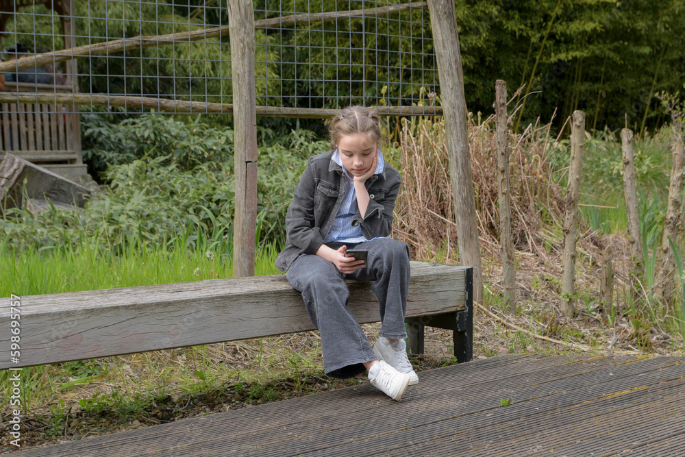 Fototapeta premium Sad message on the phone. A sad girl on a park bench reads a sad message from someone